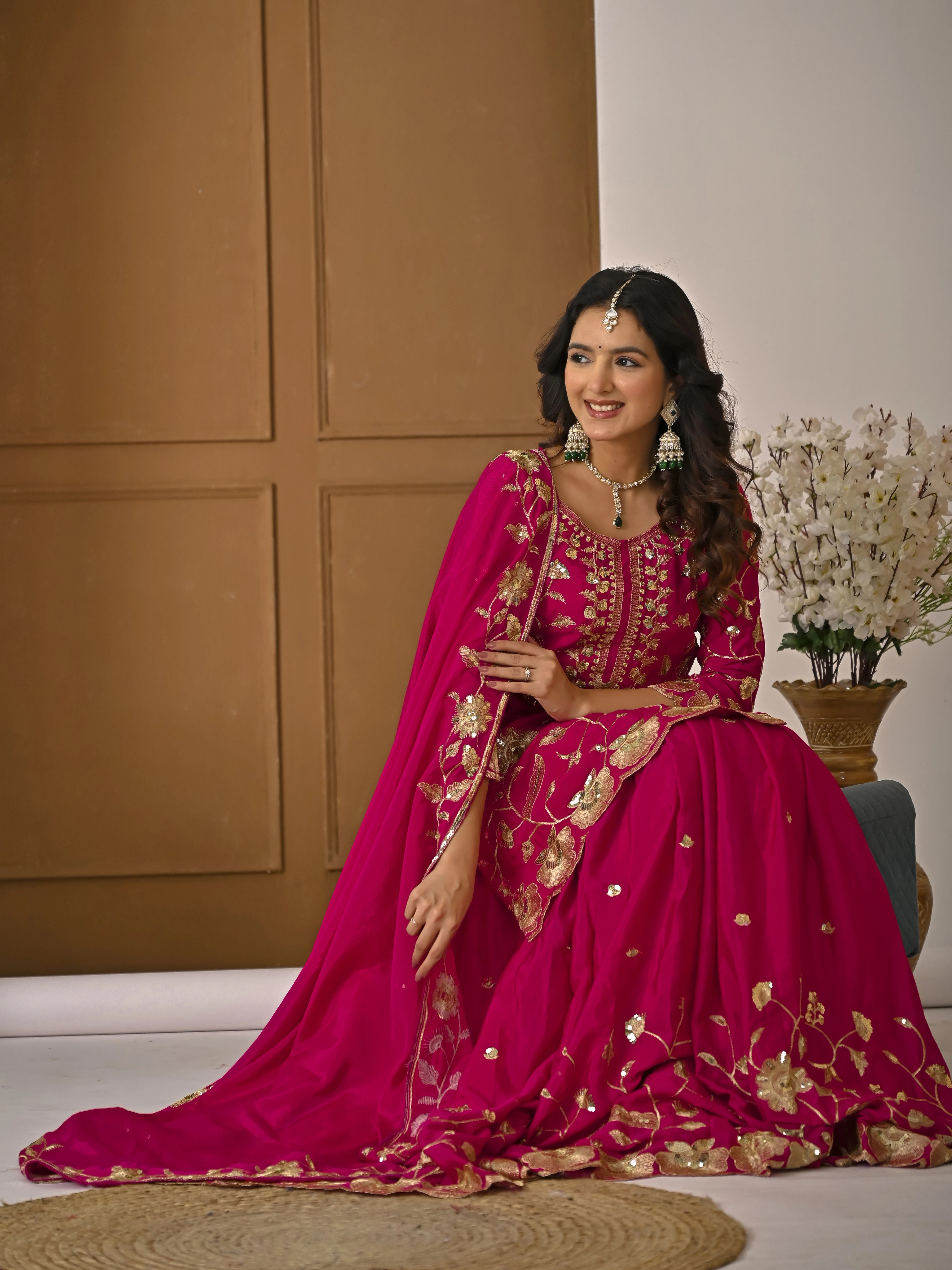 Woman in a pink traditional outfit with gold embroidery sitting on a white floor.